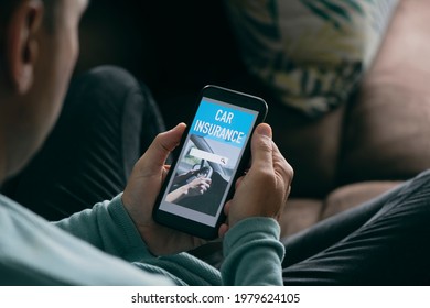 Closeup Of A Young Caucasian Man, Sitting On A Brown Sofa In His Living Room, Looking For Car Insurance Online On His Smartphone, With A Simulated Search Engine