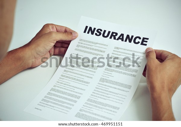 closeup of a young caucasian man sitting
at a white table reading the terms of an
insurance