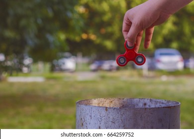 Closeup Of A Young Caucasian Man Throwing A Red Fidget Spinner In A Garbage Can On The Background Of Nature.