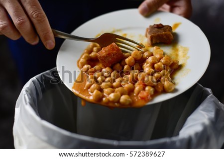 closeup of a young caucasian man throwing the leftover of a plate of chickpea stew to the trash bin