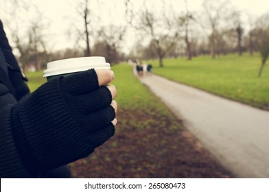 closeup of a young caucasian man very sheltered wearing fingerless gloves holds a hot drink in a paper cup in Hyde Park in winter in London, United Kingdom