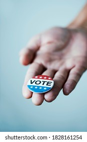 closeup of a young caucasian man with a vote badge for the United States election in his hand, on an off-white background