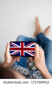 closeup of a young caucasian man, wearing casual clothes, sitting in a chair indoors, having his smartphone in his hand with the text do you speak English and the flag of UK in its screen - Shutterstock ID 1717509412
