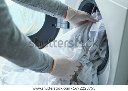 closeup of a young caucasian man, wearing latex gloves, putting white bed linen into the washing machine