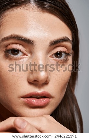 A close-up of a young Caucasian woman with mesmerizing brown eyes and flawless skin in a studio setting.