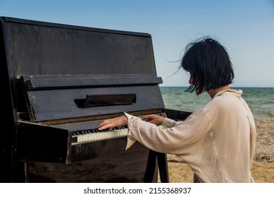 close-up of a young caucassian girl play on old black piano on the sea beach