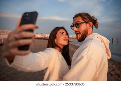 close-up of a young and charming couple of lovers taking a selfie with their smartphones while they are on the beach at sunset. The two lovers are accomplices and in love with each other. - Powered by Shutterstock