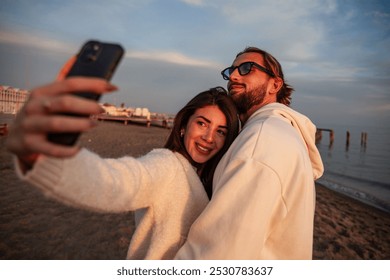 close-up of a young and charming couple of lovers taking a selfie with their smartphones while they are on the beach at sunset. The two lovers are accomplices and in love with each other. - Powered by Shutterstock