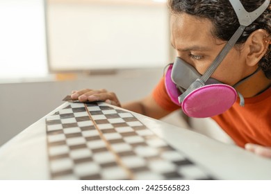 Close-up of a young concentrated man with protective work mask sanding a surfboard - Powered by Shutterstock