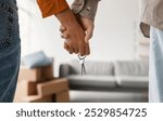 Closeup of young couple holding hands and new house key, moving in together. Unrecognizable boyfriend and girlfriend relocating to their own property, cropped view. Mortgage, real estate concept