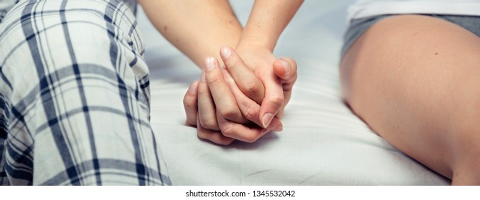 Closeup of young couple holding hands relaxing together sitting over a bed. Love and couple relationships concept.