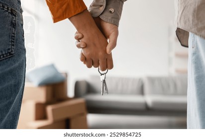 Closeup of young couple holding hands and new house key, moving in together. Unrecognizable boyfriend and girlfriend relocating to their own property, cropped view. Mortgage, real estate concept