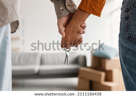 Closeup of young couple holding hands and new house key, moving in together. Unrecognizable boyfriend and girlfriend relocating to their own property, cropped view. Mortgage, real estate concept