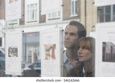 Closeup Of A Young Couple Looking Through Window At Estate Agents