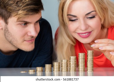 Close-up Of Young Couple Saving Money By Stacking Coins Over Table