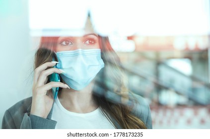 Close-up of young entrepreneurial woman talking to her smartphone through a window. She is wearing a face mask. Selective focus. Space for text. Business and new normal concept.  - Powered by Shutterstock