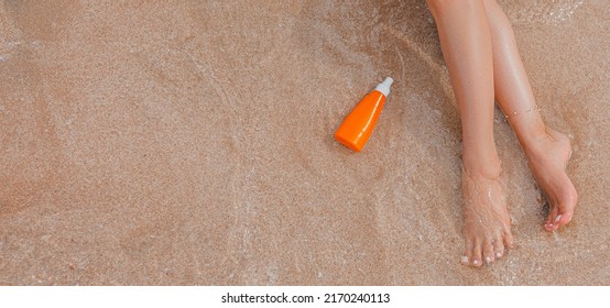 Close-up Of Young Female Bare Feet With Sunscreen Cream On Beach With A Sea Wave. Woman Uses Moisturizer, Relaxing, Enjoying Time Of Summer Vacation. Legs Of Girl On The Seaside With Sandy Background