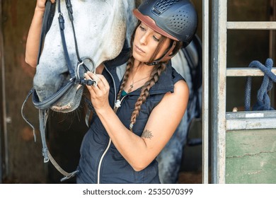 closeup young female rider wearing a helmet as she fits the bit into her horse's mouth. This intimate moment captures her careful attention and dedication to properly preparing her horse for riding - Powered by Shutterstock