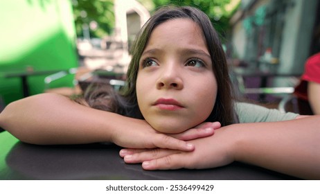 Close-up of a young girl resting her chin on her hands, gazing thoughtfully into the distance. Her expression conveys a sense of contemplation and introspection in an outdoor setting - Powered by Shutterstock