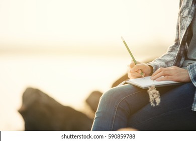 Close-up of a young girl writing into her diary, in the park,flare light