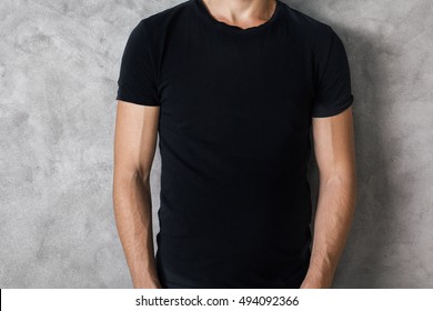 Closeup of young guy's body in empty black t-shirt on textured concrete wall background. Mock up