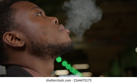 Close-up Young Handsome African American Man Smoking Cigarette In Dark Alley. Lips Blowing Smoke On Black Background. Portrait Gangster Smokes Marijuana Or Cannabis At Night In City.