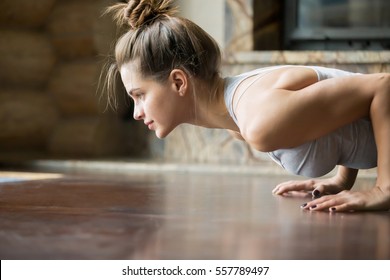 Closeup of young happy attractive woman practicing yoga, doing four limbed staff, push ups or press ups exercise, chaturanga dandasana pose, working out, wearing sportswear, bra, indoor, home interior - Powered by Shutterstock