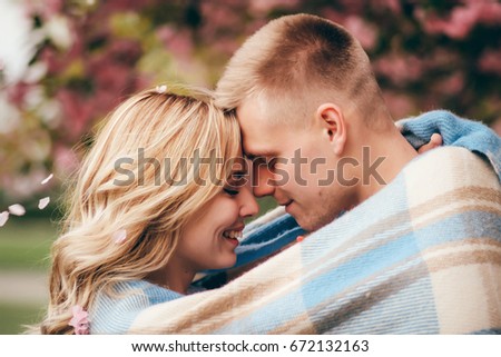 Closeup of young happy couple laughing under blanket in a cold day with sea and dark cloudy sky on the background They stand under blooming cherry