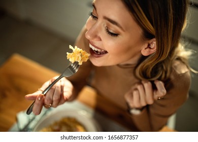 Close-up of young happy woman eating pasta at dining table. 