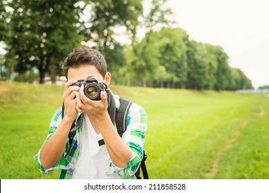 Closeup of young hipster man with digital camera outdoors. Young male photographer photographing nature on summer day. - Powered by Shutterstock