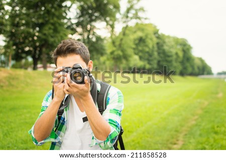 Closeup of young hipster man with digital camera outdoors. Young male photographer photographing nature on summer day.