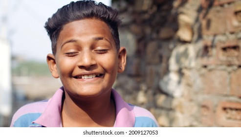 A Closeup Of A Young Indian Boy Grinning At The Camera With His Eyes Closed On A Blurry Background