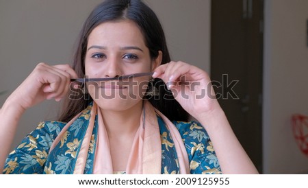 A closeup of a young Indian woman in traditional clothing making a sillmustache out of her hair
