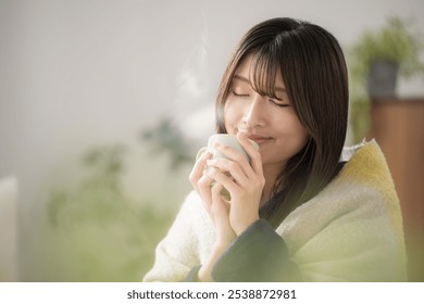 Close-up of a young Japanese (Asian) woman with eyes closed relaxing in a winter living room drinking a hot beverage - Powered by Shutterstock