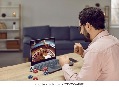 Close-up of young joyful man playing roulette. Lucky guy bets at online casino at home on his laptop. Winning Russian roulette over the Internet on the net. - Powered by Shutterstock