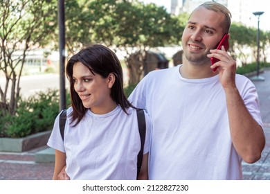 Close-up Of A Young Latin Couple Walking While The Man Talks On The Cell Phone. Concept IT, Comunications.