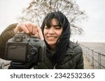 closeup young latin woman vlogger happy smiling pressing the record button on her digital DSRL camera to make a video standing on the pier