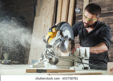 Close-up as a young male construction worker carpenter saws a circular saw blade, sawdust fly in the workshop