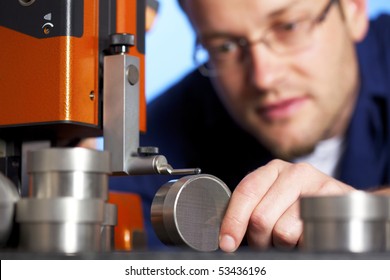 Close-up of young male engineer in blue overall taking precision measurement of metal parts with micrometer, isolated on blue background.