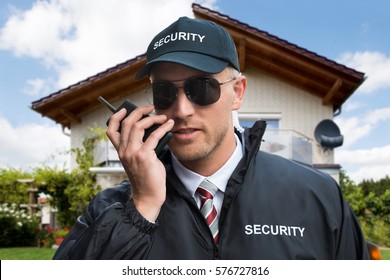 Close-up Of A Young Male Security Guard Using Walkie-talkie In Front Of A House