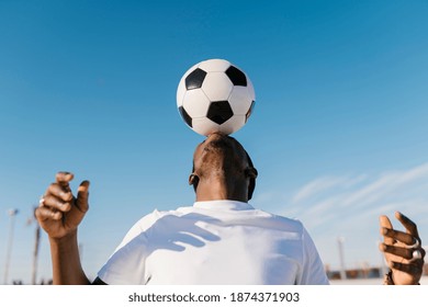 Close-up of young man balancing soccer ball on head against blue sky स्टॉक फ़ोटो