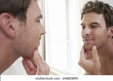 Closeup of a young man examining his stubble in mirror - Powered by Shutterstock