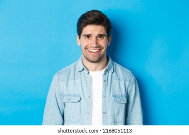 Close-up Of Young Man Feeling Awkward, Smile And Cringe From Uncomfortable Situation, Standing Over Blue Background