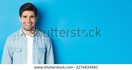 Close-up of young man feeling awkward, smile and cringe from uncomfortable situation, standing over blue background. Foto d'archivio © 