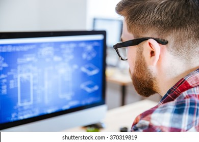 Gros plan sur un jeune homme en lunettes avec une barbe faisant des plans sur ordinateur
