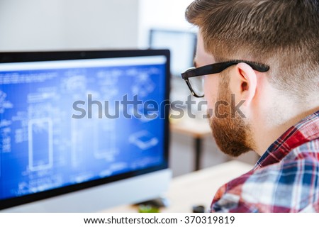Closeup of young man in glasses with beard making blueprints on computer