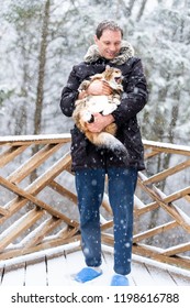 Closeup Of Young Man Holding Angry, Scared Meowing Maine Coon Cat Outside, Outdoors In Park In Snow, Snowing Weather During Snowstorm, Storm With Snowflakes, Flakes Falling