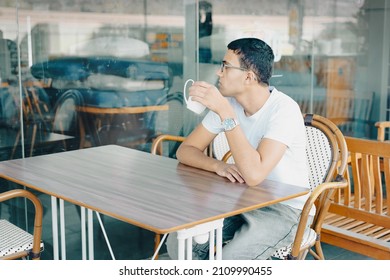 Close-Up Of Young Man Holding Coffe Cup In Cafe. Teenager In A Cafe Drinking Cup Of Tea, Deep In Thought.