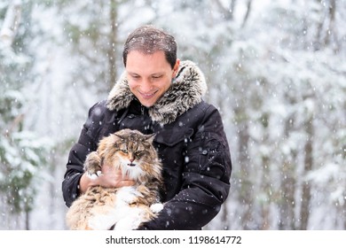 Closeup Of Young Man Holding Meowing Maine Coon Cat Outside, Outdoors In Park In Snow, Snowing Weather During Snowstorm, Storm With Snowflakes, Flakes Falling