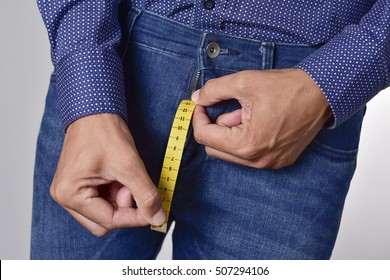 closeup of a young man holding a piece of measuring tape that is popping up from the fly of his jeans, depicting the normal range of the penis